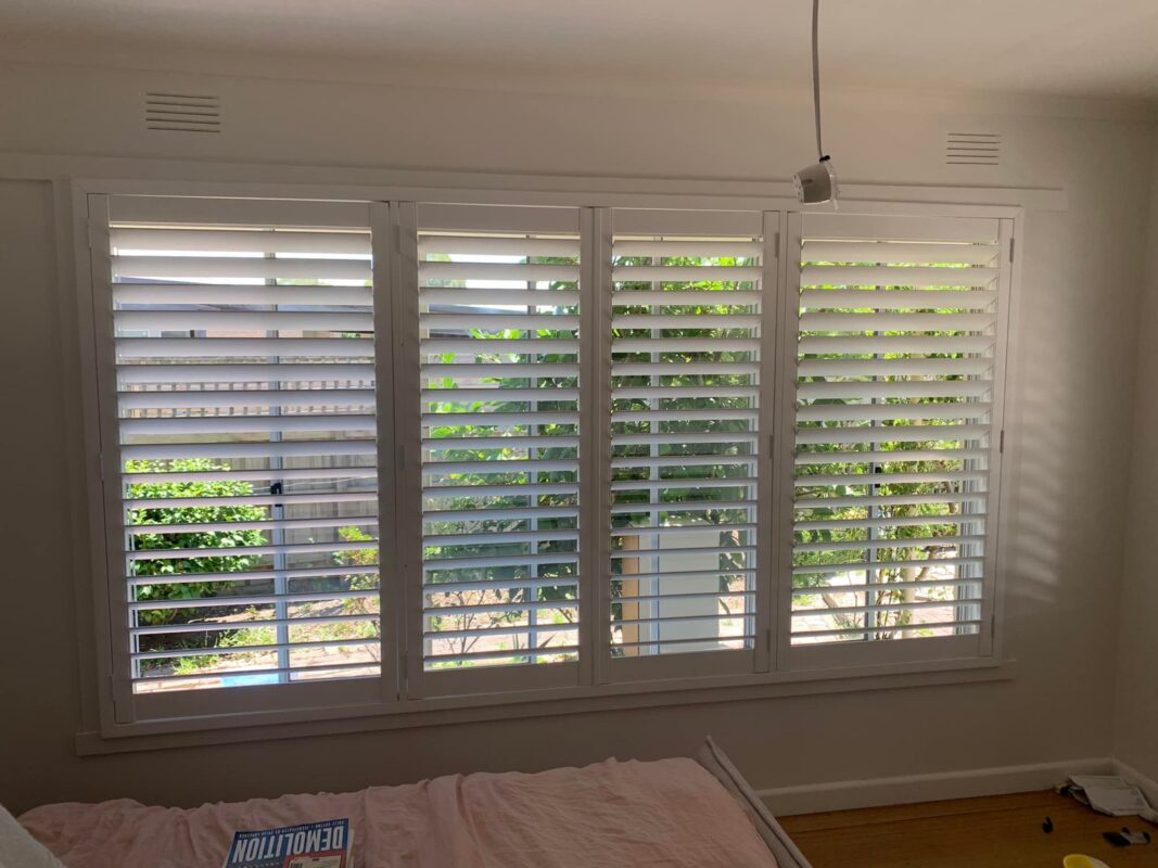 White plantation shutters across a wide four-panel bedroom window