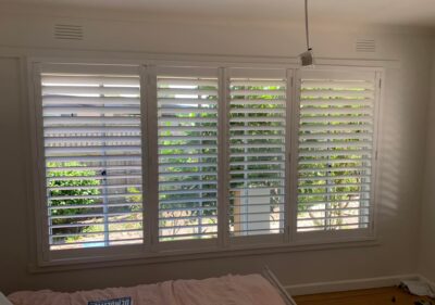 White plantation shutters across a wide four-panel bedroom window