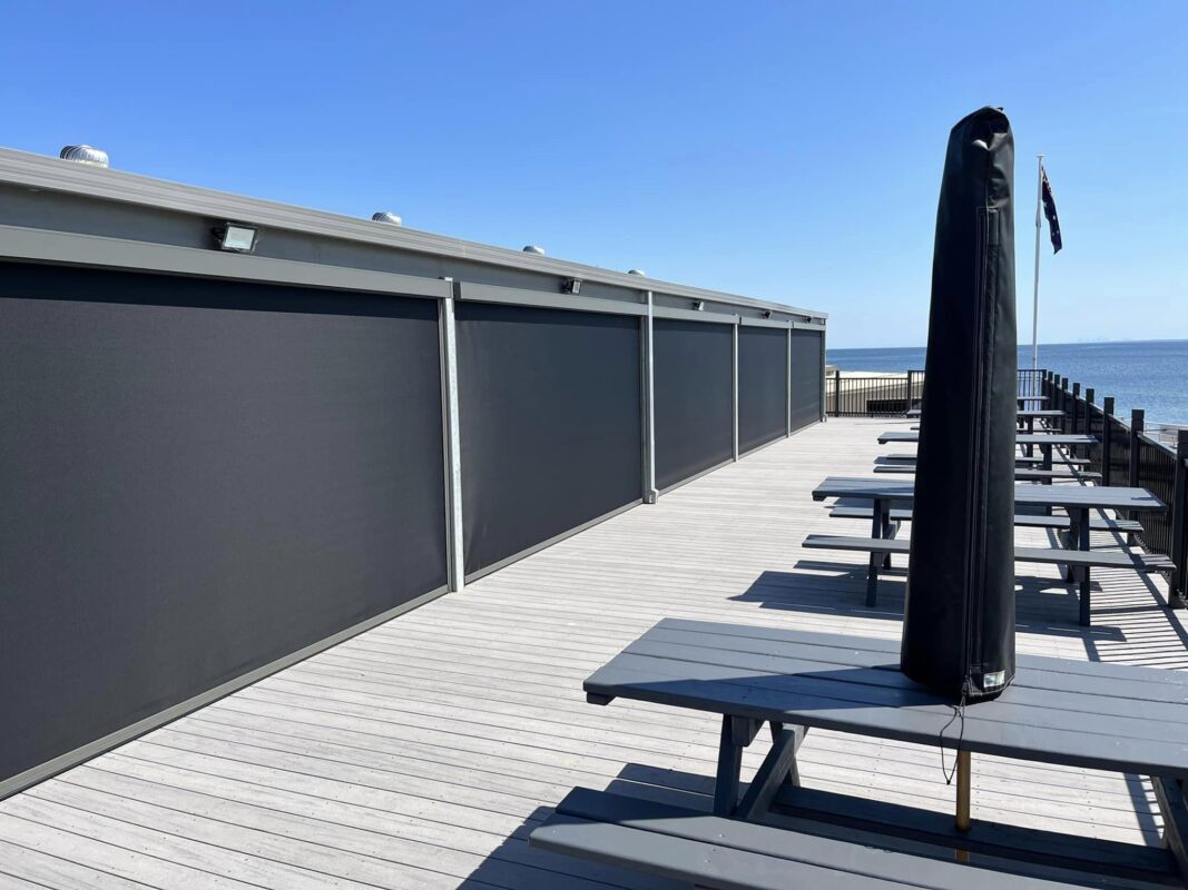Zipscreen outdoor blinds sheltering a beachfront deck with picnic tables and water views