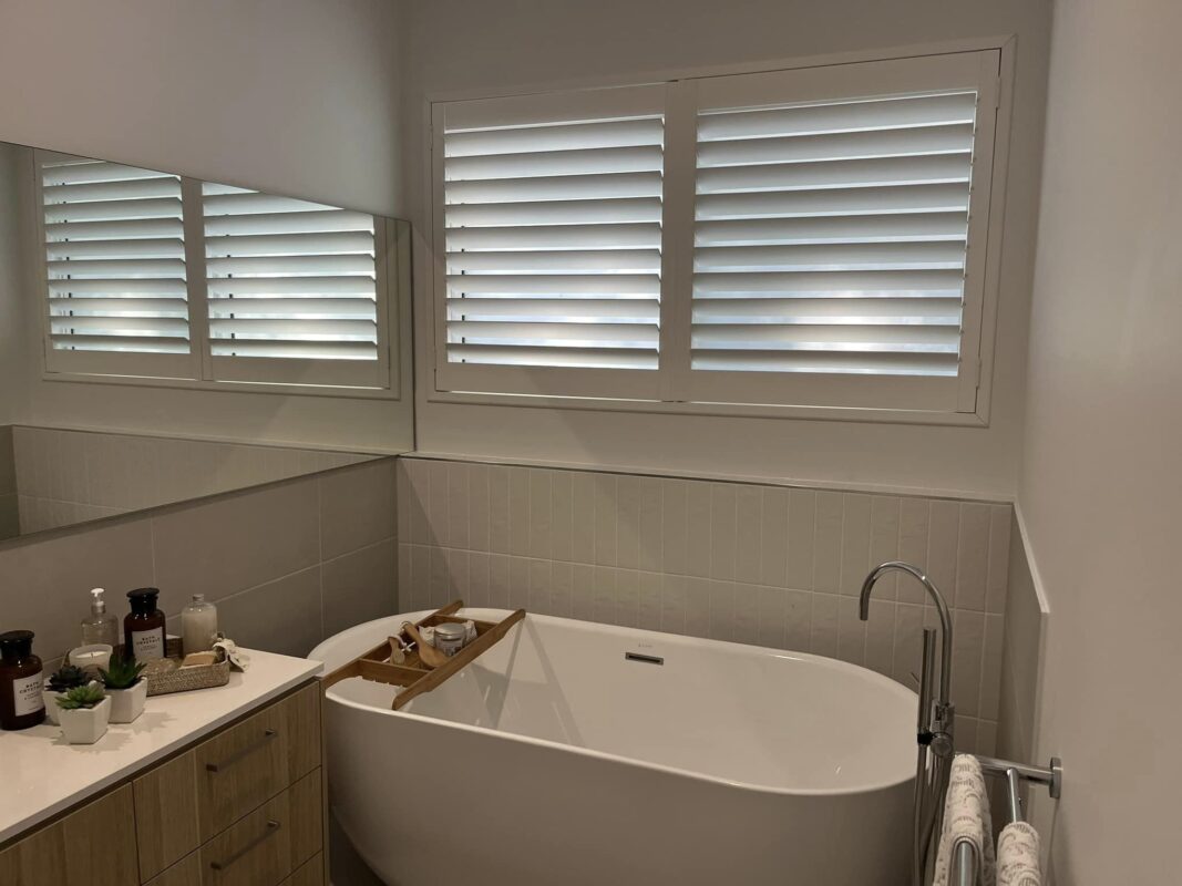 White plantation shutters above a freestanding bath in a bathroom