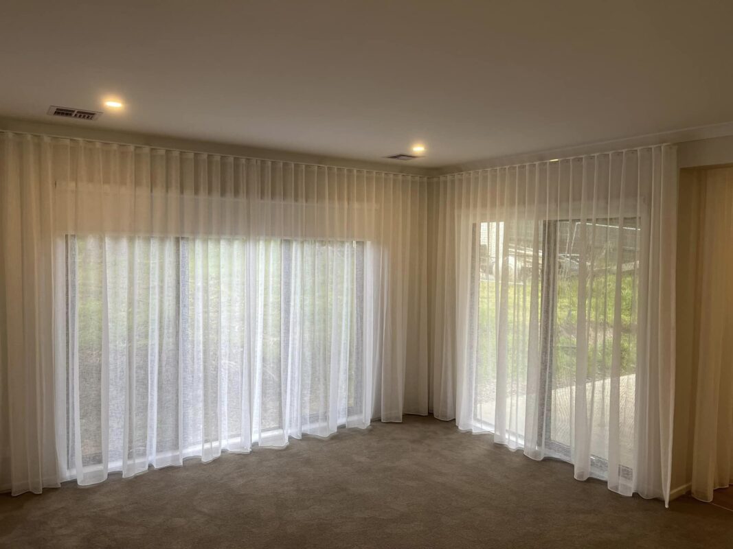 White S-Fold sheer curtains wrapping a corner window in a carpeted living room